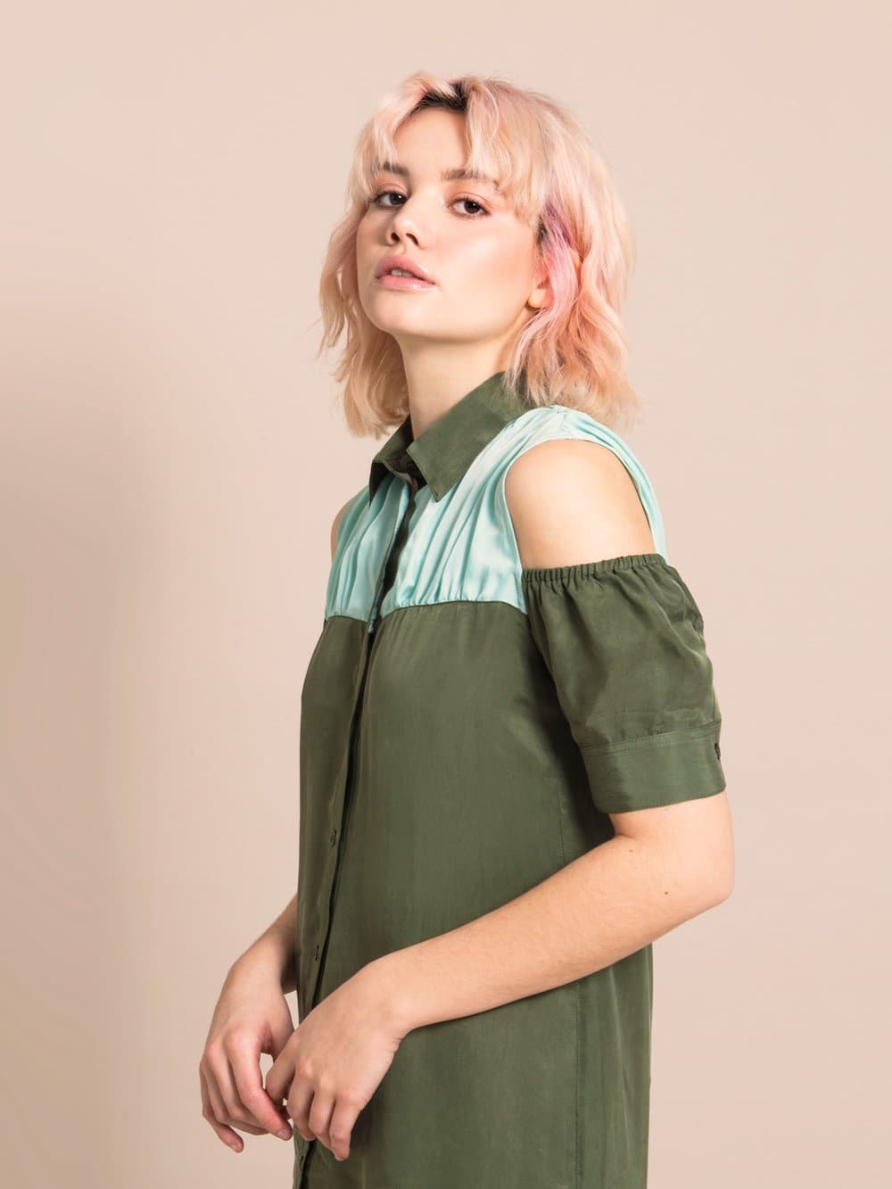 Close-up of a woman wearing a sustianable, cold-shoulder military green dress with  a collar