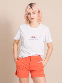 Frontshot of a woman wearing a white tee with print and orange sustainable shorts with crease