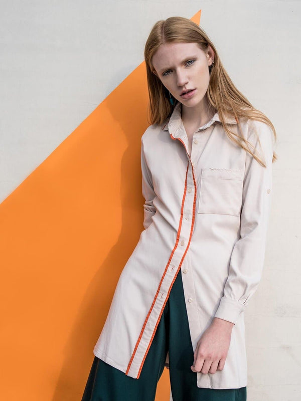 Woman wearing a beige oversized shirt with orange piping around the buttons