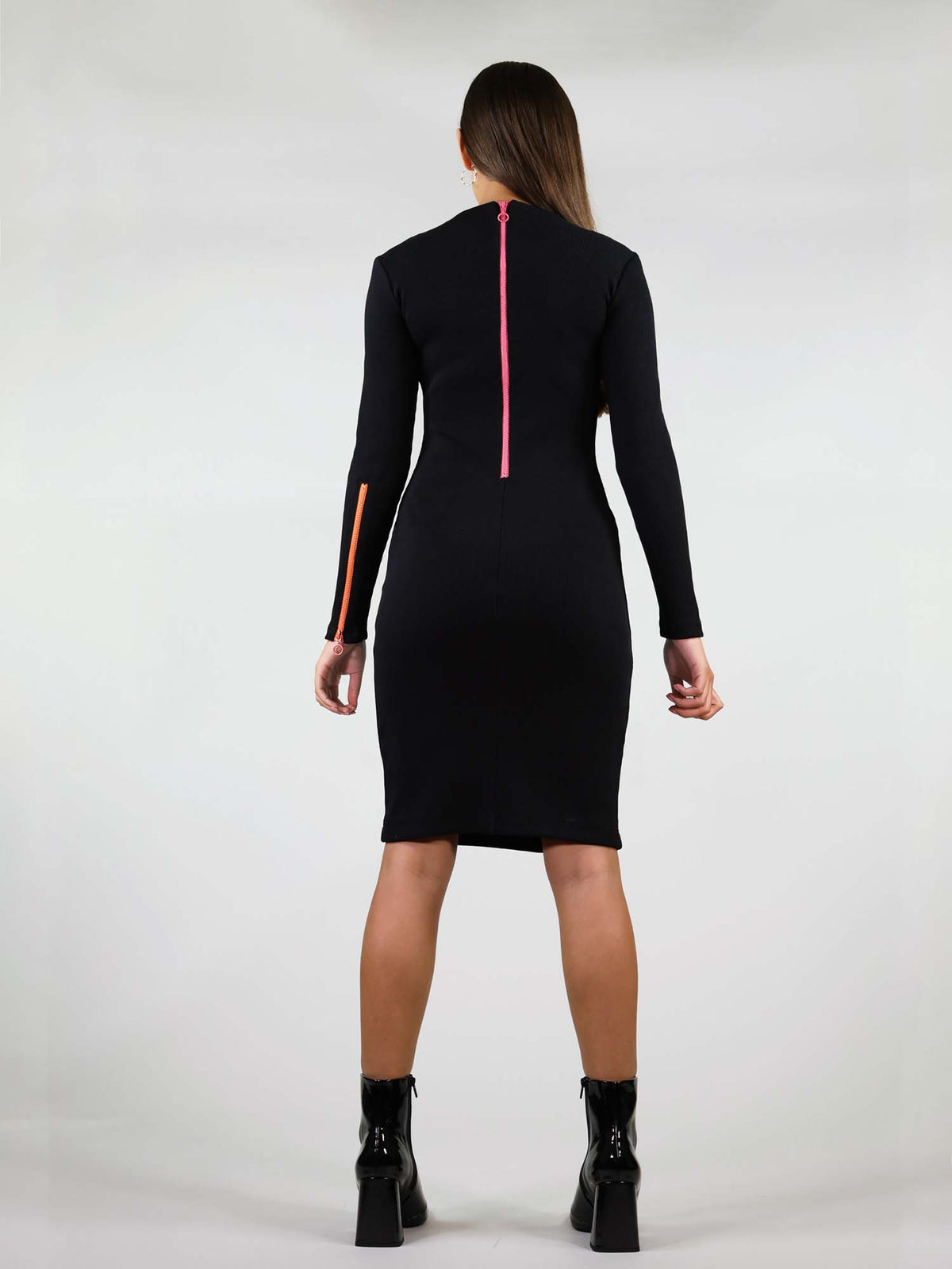 Back of the wicked zip dress in size XS has body con fit and comes in black. It has under knee length, long sleeves and two zippers. A pink zipper going from the neck to waist and a orange zipper on the left arm that unzips.