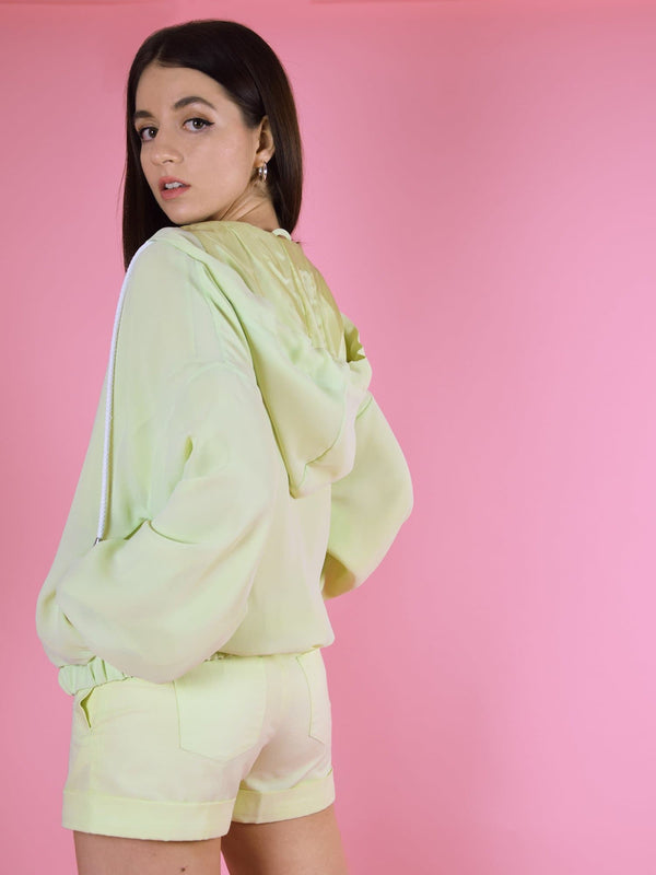 Backshot of blonde gone rogue's bonfire bomber jacket in green. The jacket is made from chiffon, has a lightweight, a hood and side pockets.