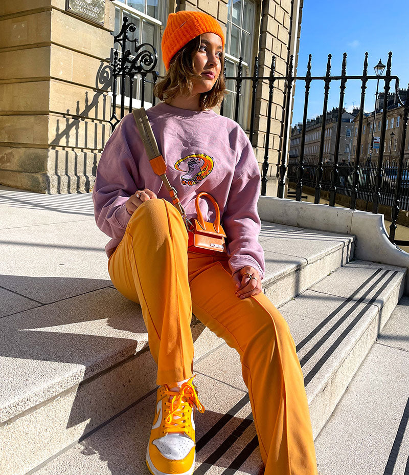 Woman sitting on stairs in the winter sunshine and wearing a purple sweatshirt and orange trousers.
