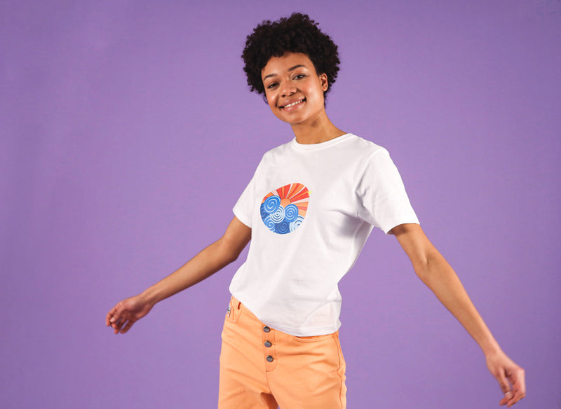 Young woman wearing a white t-shirt with print and orange jeans standing in front of a purple background.