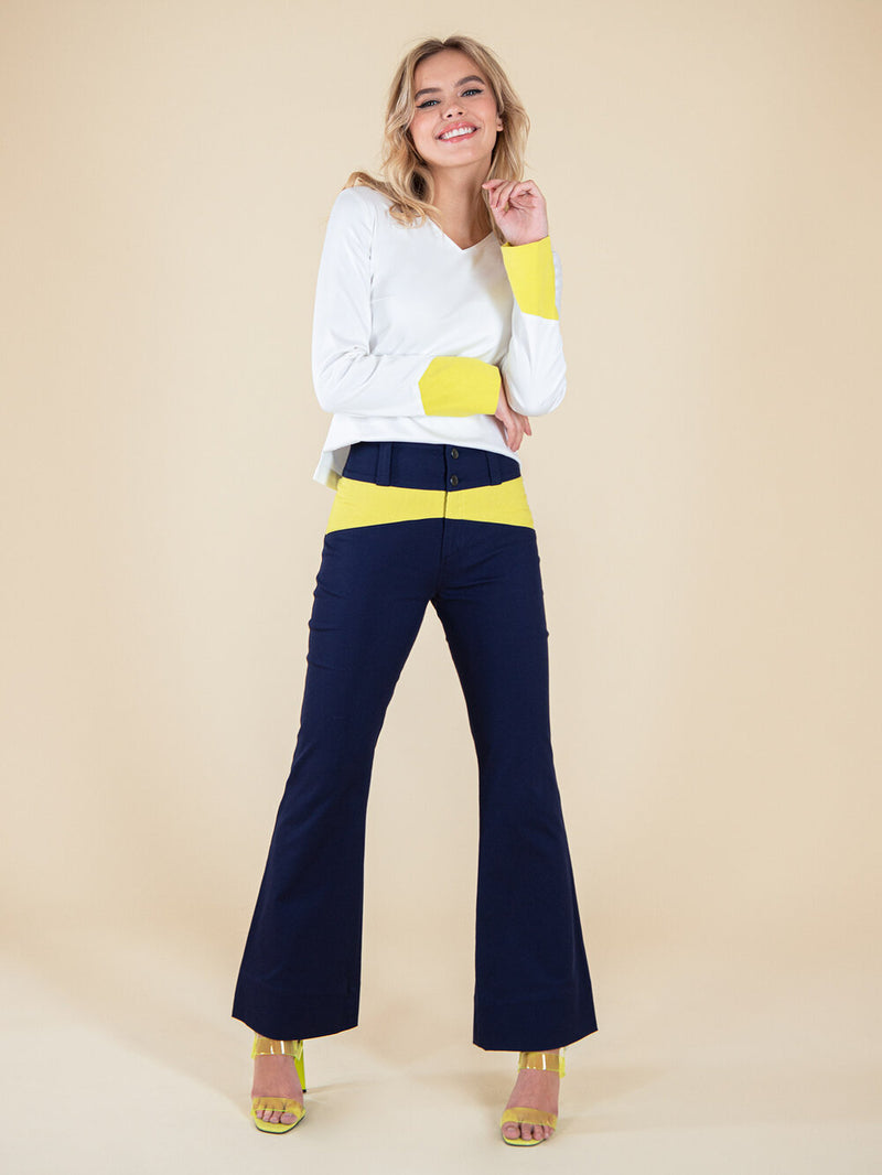 Frontshot of a woman wearing a white blouse and navy blue flared trousers with neon yellow elements
