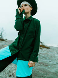 Woman in nature wearing a dark military green oversized shirt with a blue element