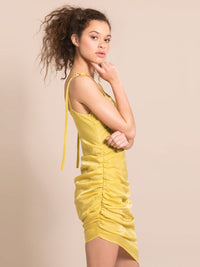 Sideshot of a model wearing a sustainable yellow silky coctail dress with gathers on the side and adjustable shoulder straps