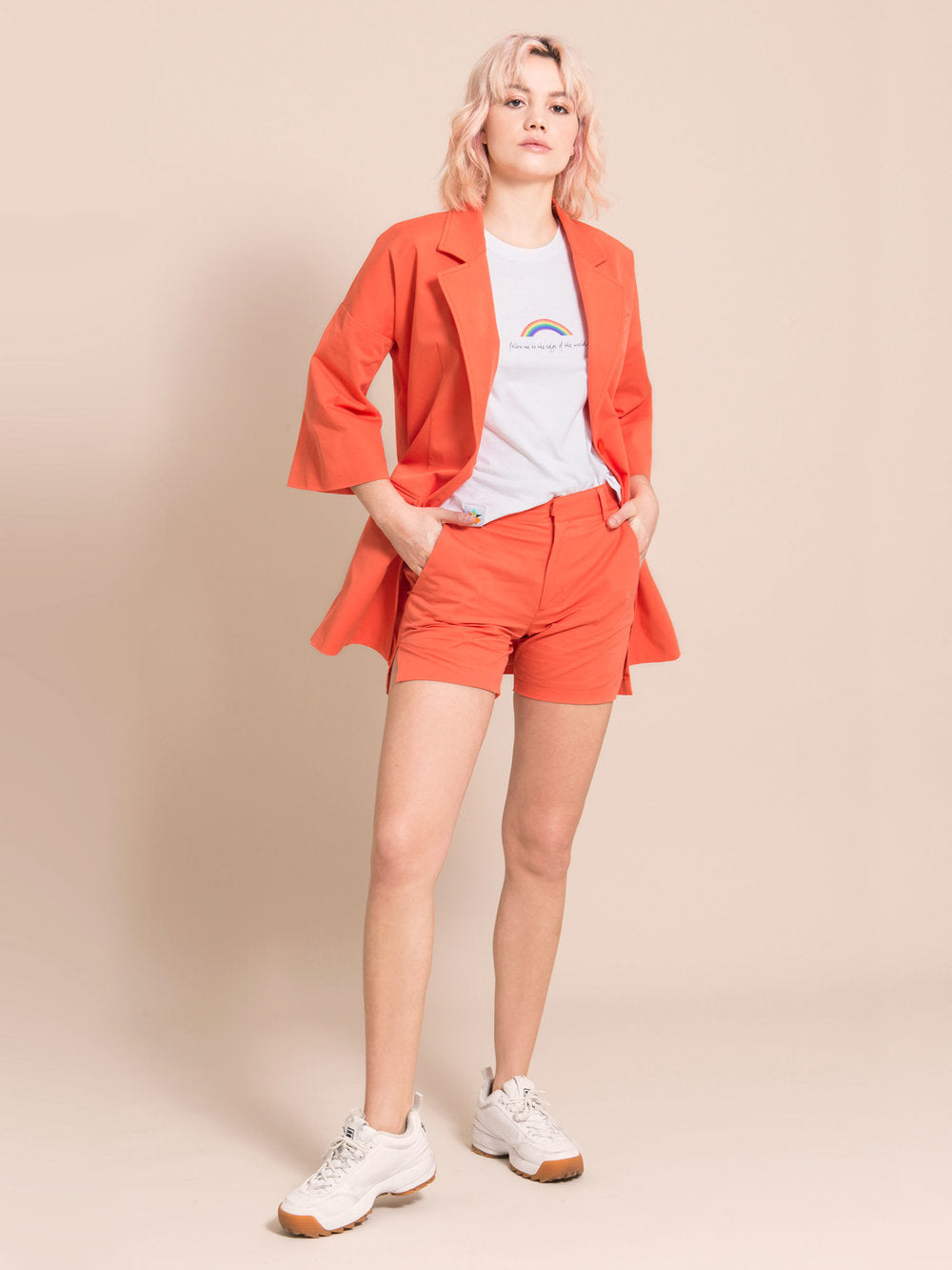 Woman wearing sustainable orange shorts with crease, white tee with print and an orange blazer with bell sleeves