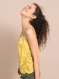 Sideshot of a happy woman wearing a sustainable yellow top with gathers on the side