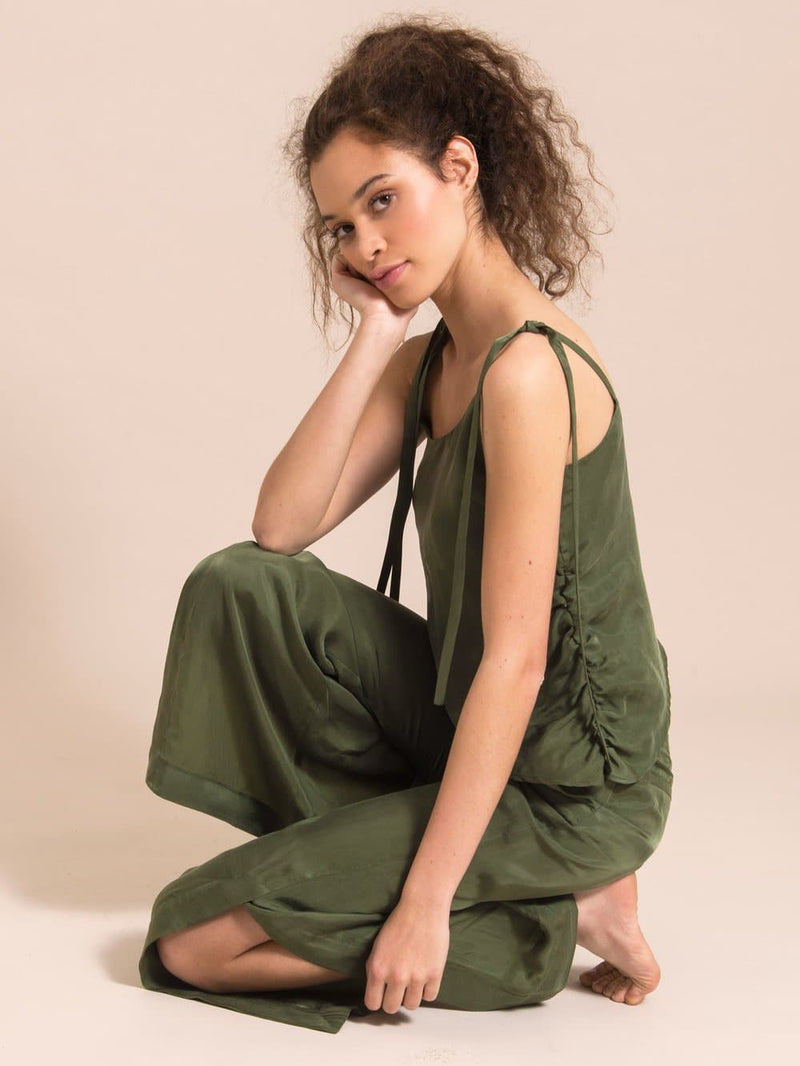 Girl sitting on the floor dressed in a sustainable dark green sleeveless top and flared trousers with slit