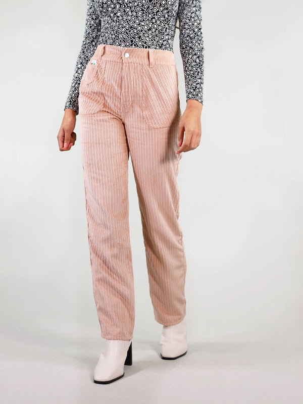 Close up view of the corduroy trousers in pastel pink. These have straight leg fit and hight waist with large side pockets. Signature logo on the left front and belt loops.