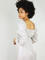 Close up shot of the back of midi empire dress in silver. Backless square design and loose fit. Long sleeve and elastic around shoulders and cuffs.