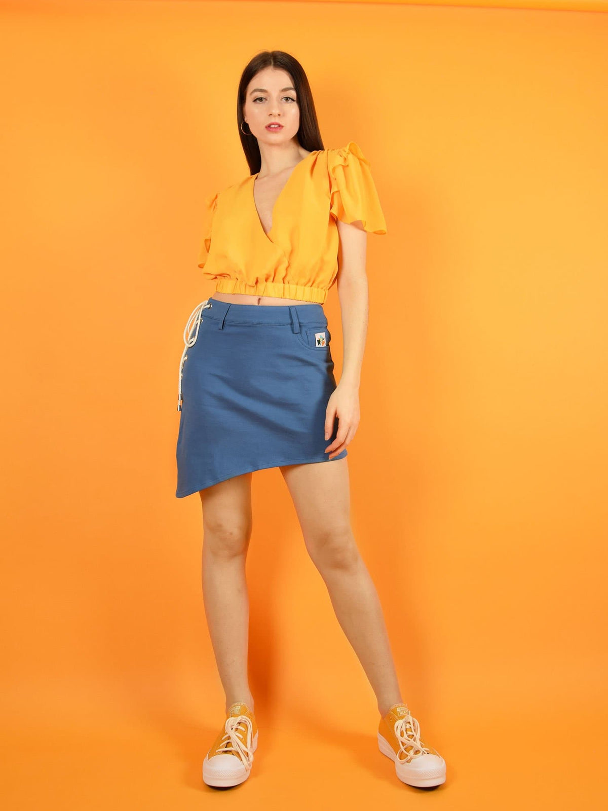 Frontshot of a cool outfit by blonde gone rogue - the wildflower surplice crop top in orange and the lace up sustainable denim skirt.